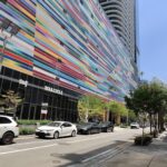 Ray-Ban Meta Wayfarer smart glasses photographed outdoors against a colorful facade.