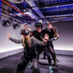 Guests in Sandbox VR free-roam kits with headsets, haptic vests, and full-body tracking markers