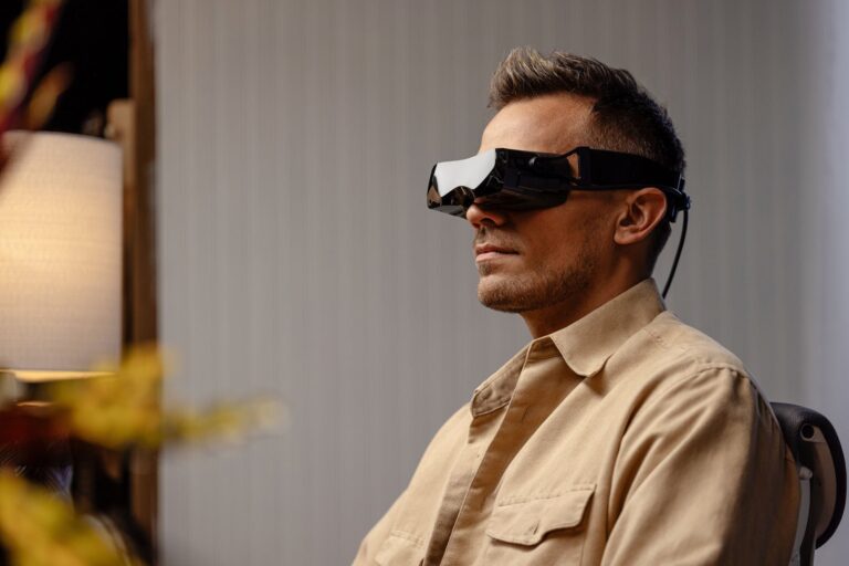Person seated indoors wearing a Bigscreen Beyond 2 VR headset with its tethered cable