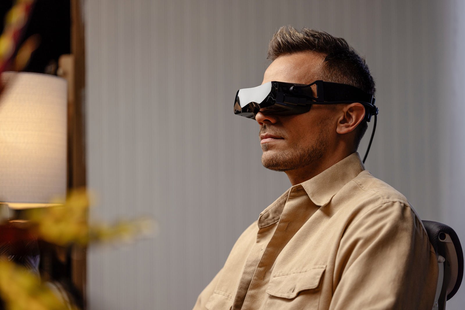 Person seated indoors wearing a Bigscreen Beyond 2 VR headset with its tethered cable