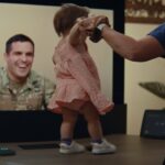A deployed U.S. Army officer smiles on a Google Beam 3D video call as his one-year-old daughter practices walking, from Google's USO docuseries