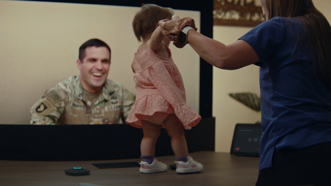 A deployed U.S. Army officer smiles on a Google Beam 3D video call as his one-year-old daughter practices walking, from Google's USO docuseries