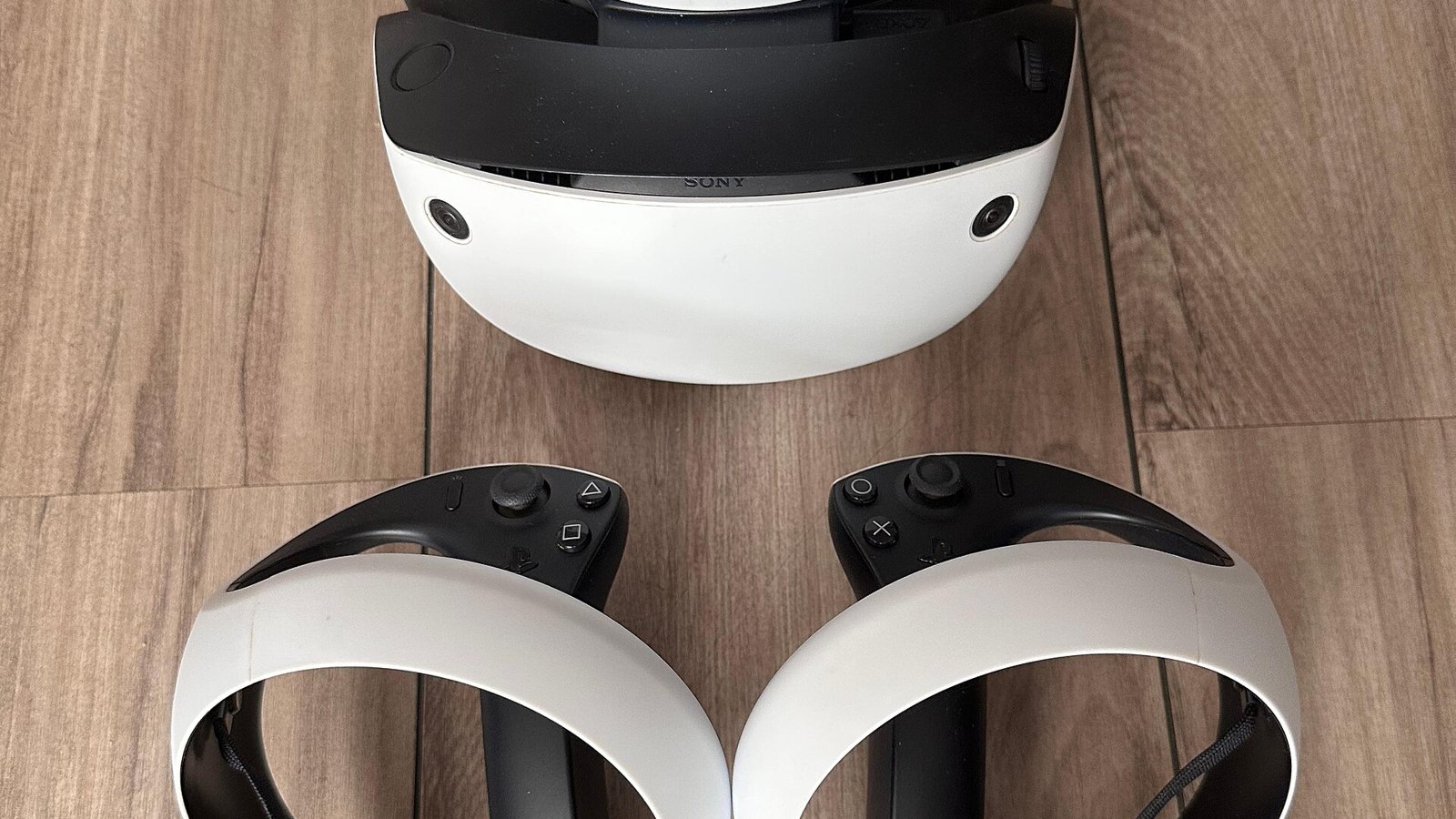 Sony PlayStation VR2 headset and two PS VR2 Sense controllers on a wooden floor