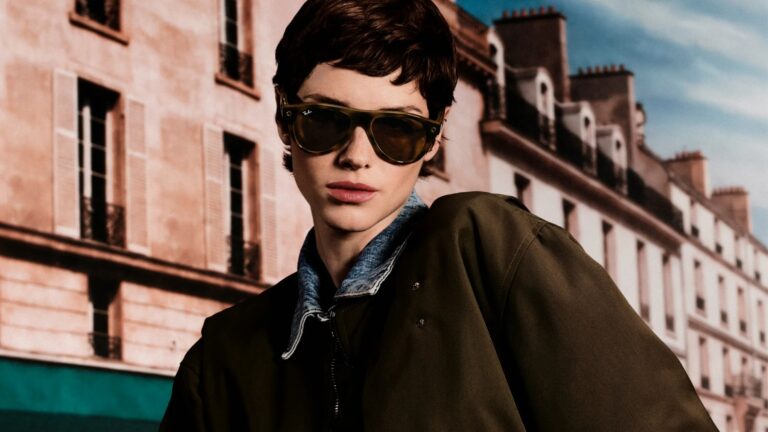 Model wearing olive-framed Ray-Ban Meta Gen 3 AI glasses with tinted lenses in front of a Paris building