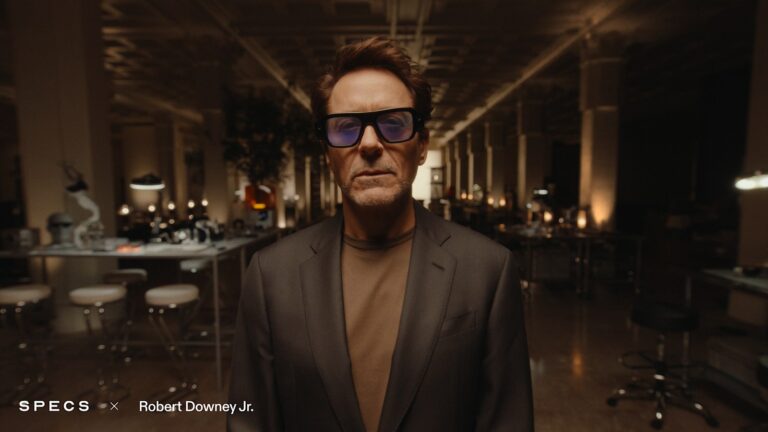 Robert Downey Jr. wearing Snap SPECS augmented reality glasses in a dim workshop, from Snap's October 20, 2026 announcement